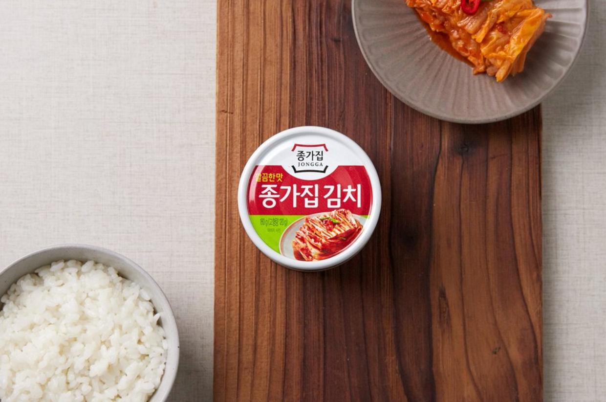 korean brand jongga canned kimchi on wooden plank with a bowl of rice and kimchi