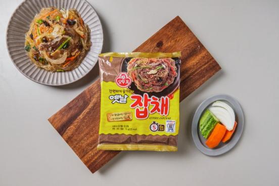 korean brand ottogi's Japchae pack on wooden platter with a plate of japchae and a plate of vegetables on side