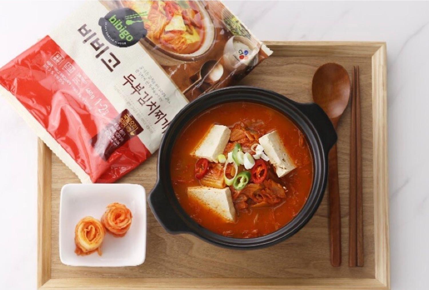 korean brand bibigo's tofu kimchi jjigae on a tray with kimchi and cutlery