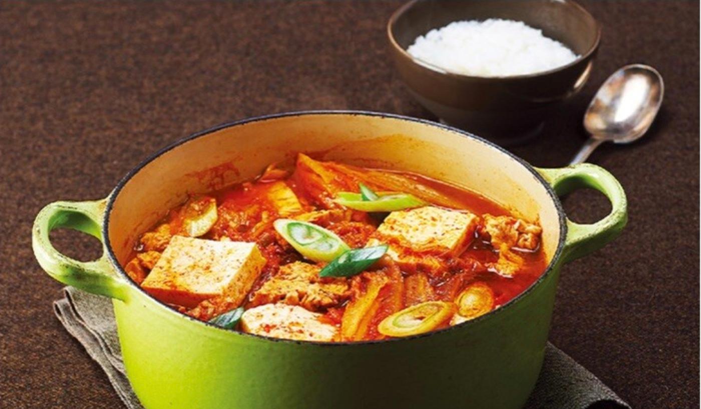 tofu kimchi jjigae in a green pot with a bowl of rice in the background