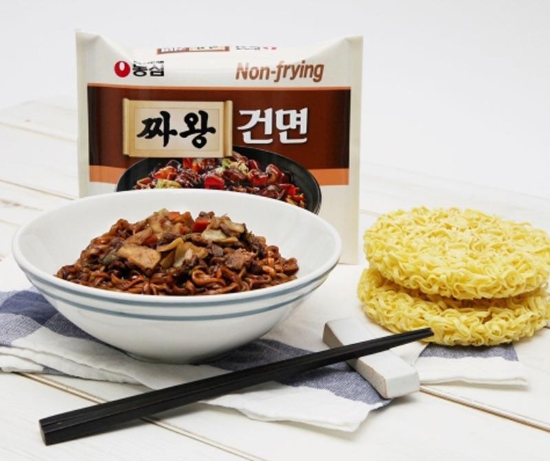 Korean brand nongshim's Jjawang Mild pack next to prepared bowl topped and raw ramen noodles