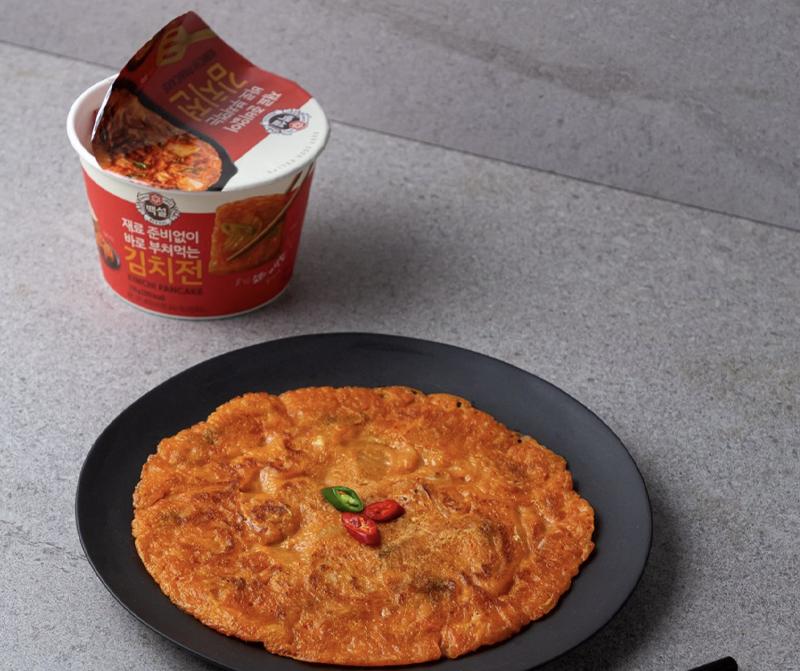 korean brand beksul's kimchi pancake instant cup mix open container next to plate of kimchi pancake 