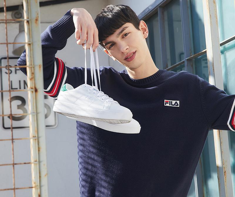model holding up fila korea court plumpy sneakers in white and green by the laces 