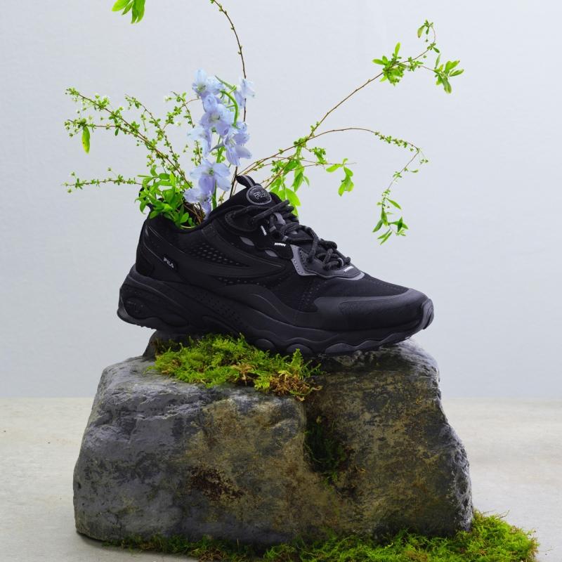 fila korea bubble tr in black on top of mossy rock with flowers and twigs coming out of the shoe 